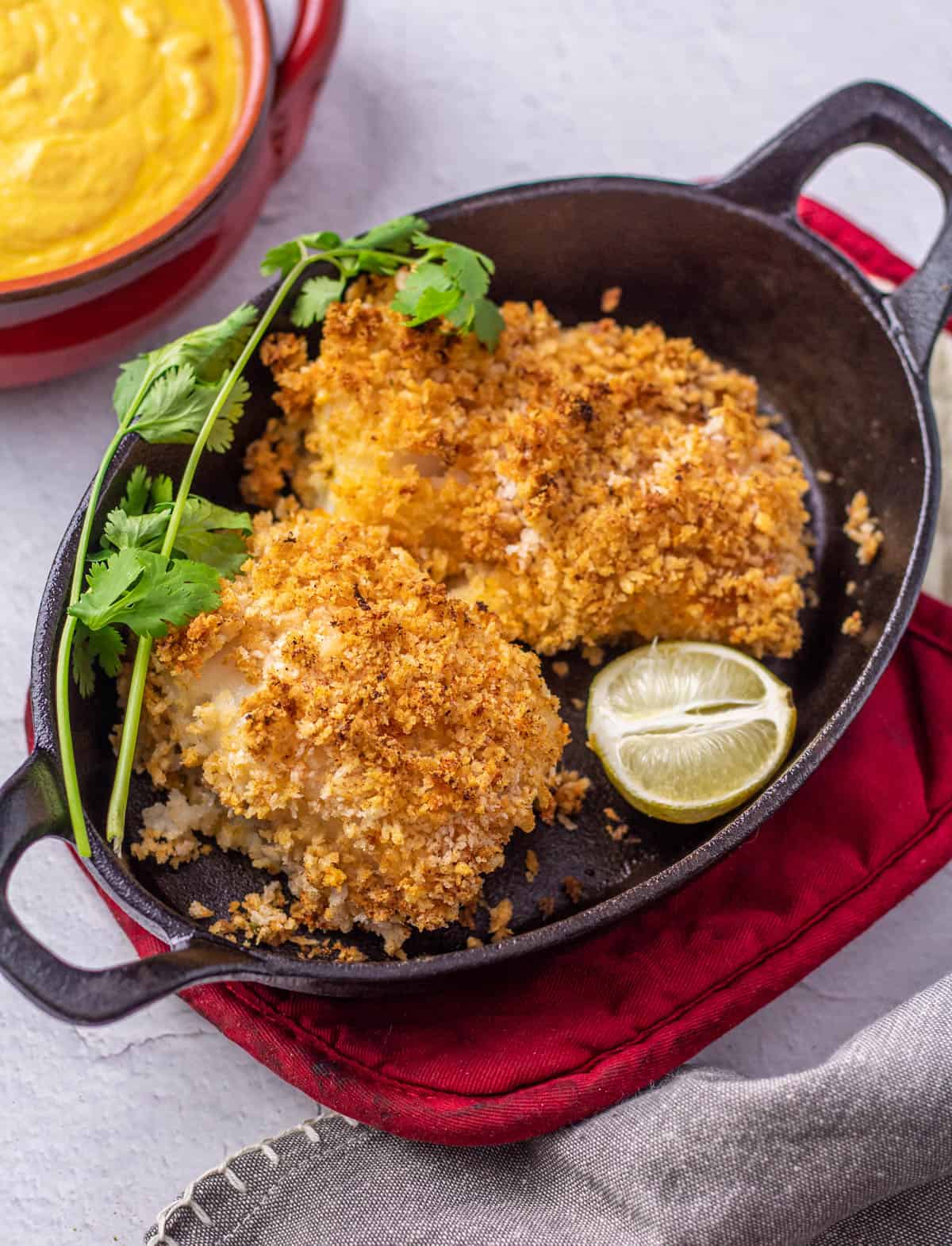Panko crusted cod in a cast iron dish with a container full of huancaina sauce.