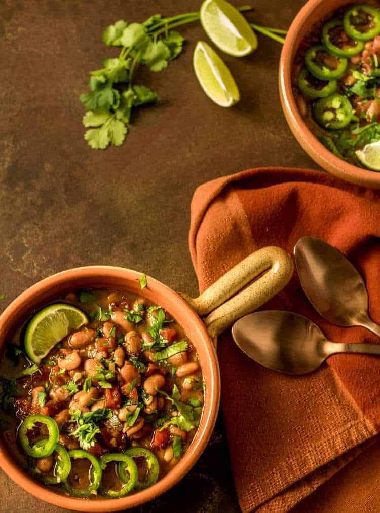 Instant Pot Vegan Borracho beans in a bowl with lime wedge, sliced jalapenos and cilantro.