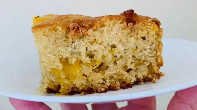 Hand holding a white plate with a slice of mango bread.