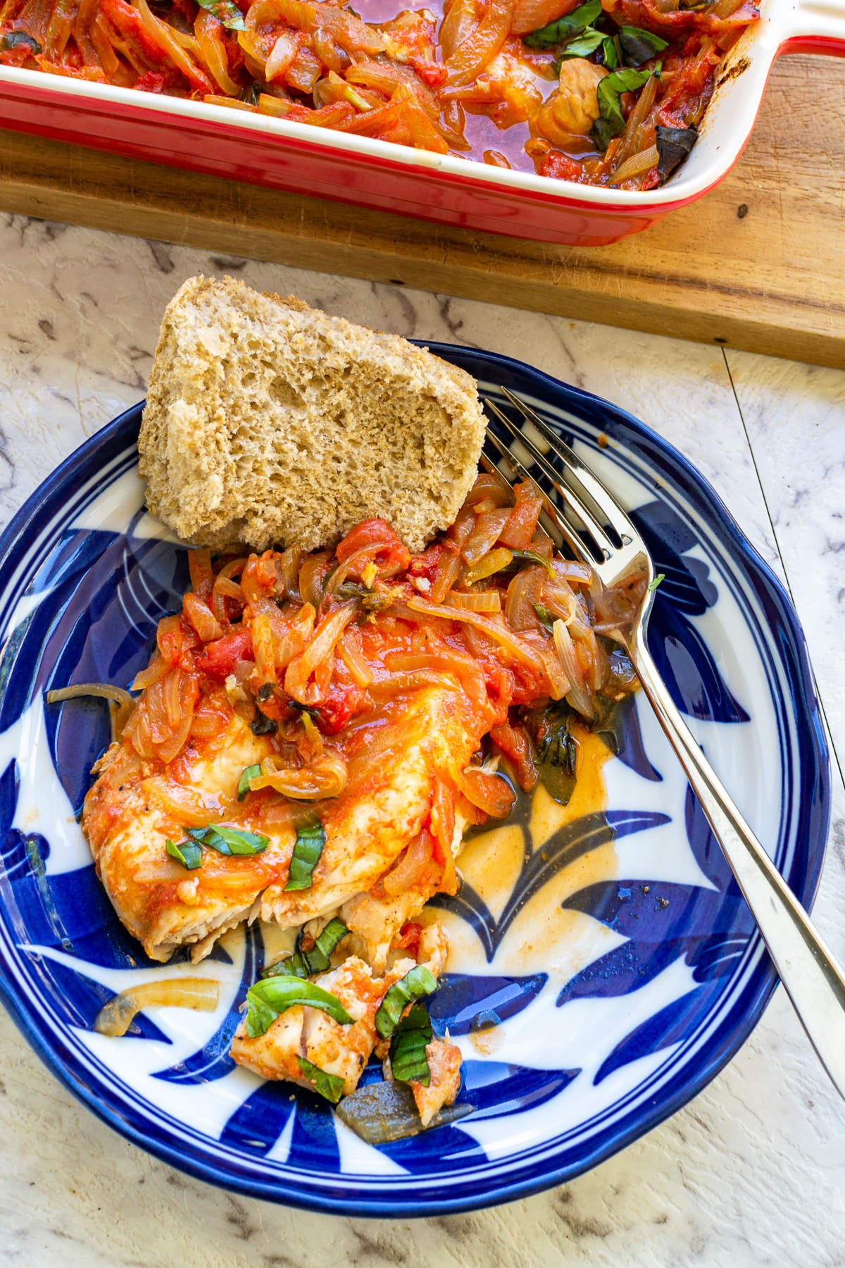 Greek oven baked fish on a decorative blue and white plate with a fork and bread.