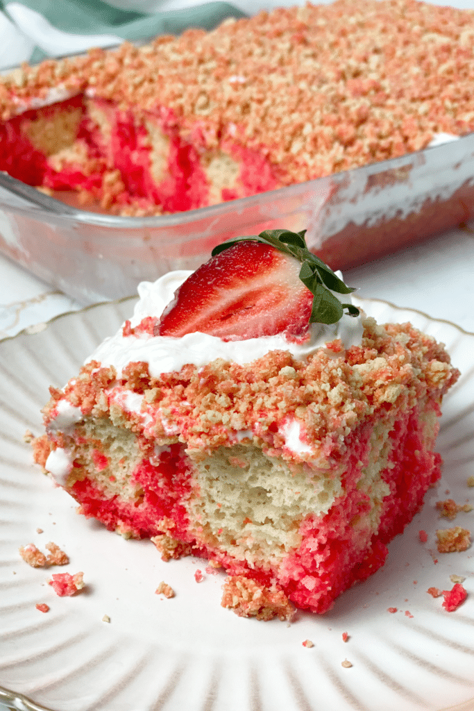 Strawberry crunch poke cake in a glass dish with a serving on a white plate.