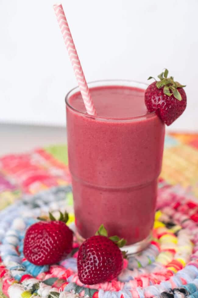 Strawberry banana protein smoothie in a glass with strawberries on a colorful mat.