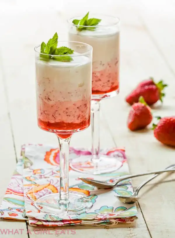 Strawberry parfaits served in dessert glasses with strawberries and spoons surrounding it.