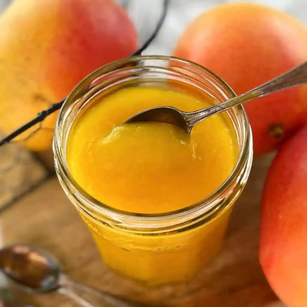 Mason jar filled with mango coulis with spoon in it.