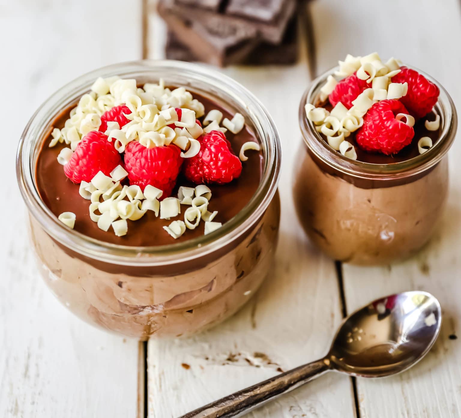 Chocolate cheesecake mousse in jars with spoon and chocolate in background.