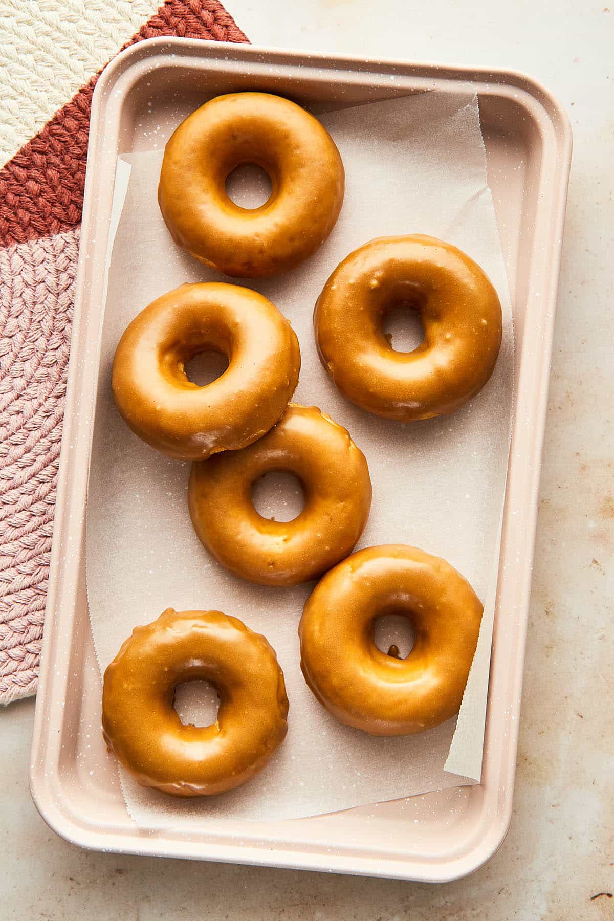 Maple glazed donuts on parchment paper in a baking tray.