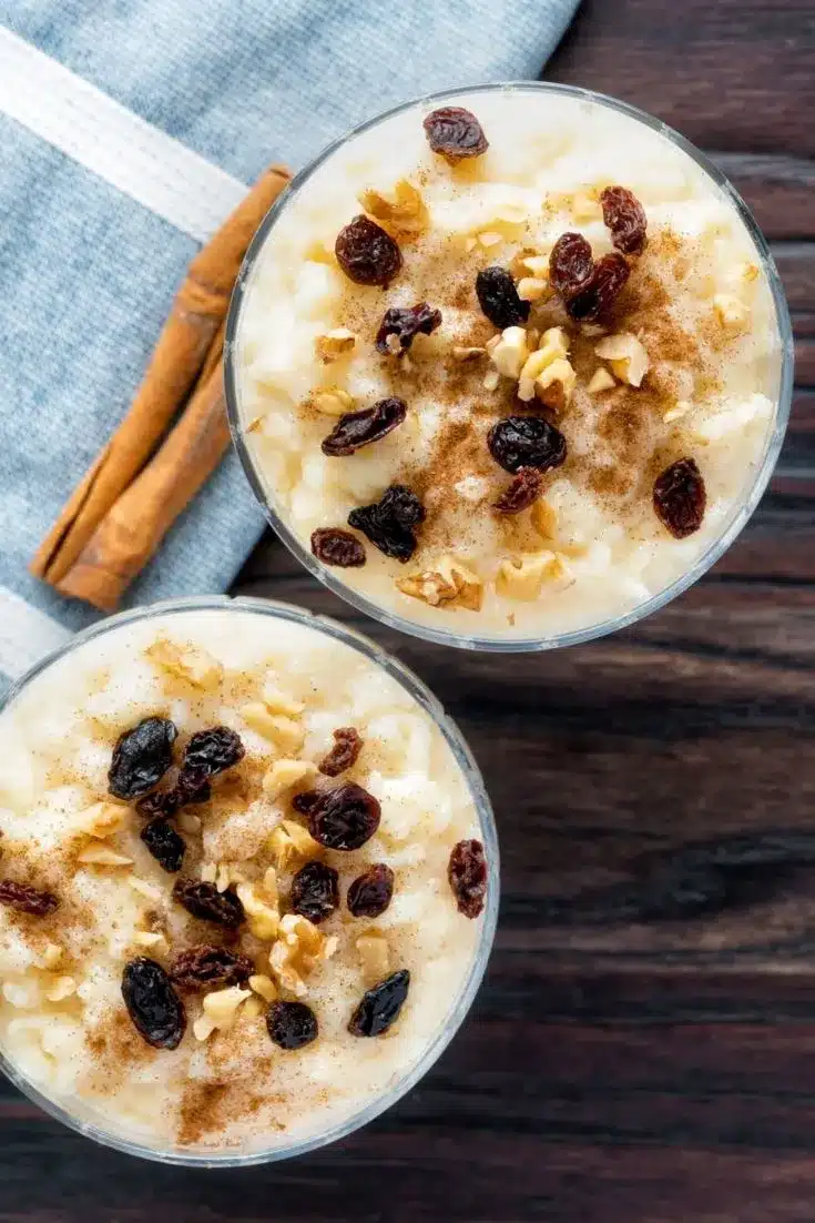 Two servings of Mexican rice pudding with cinnamon sticks and towel in background.