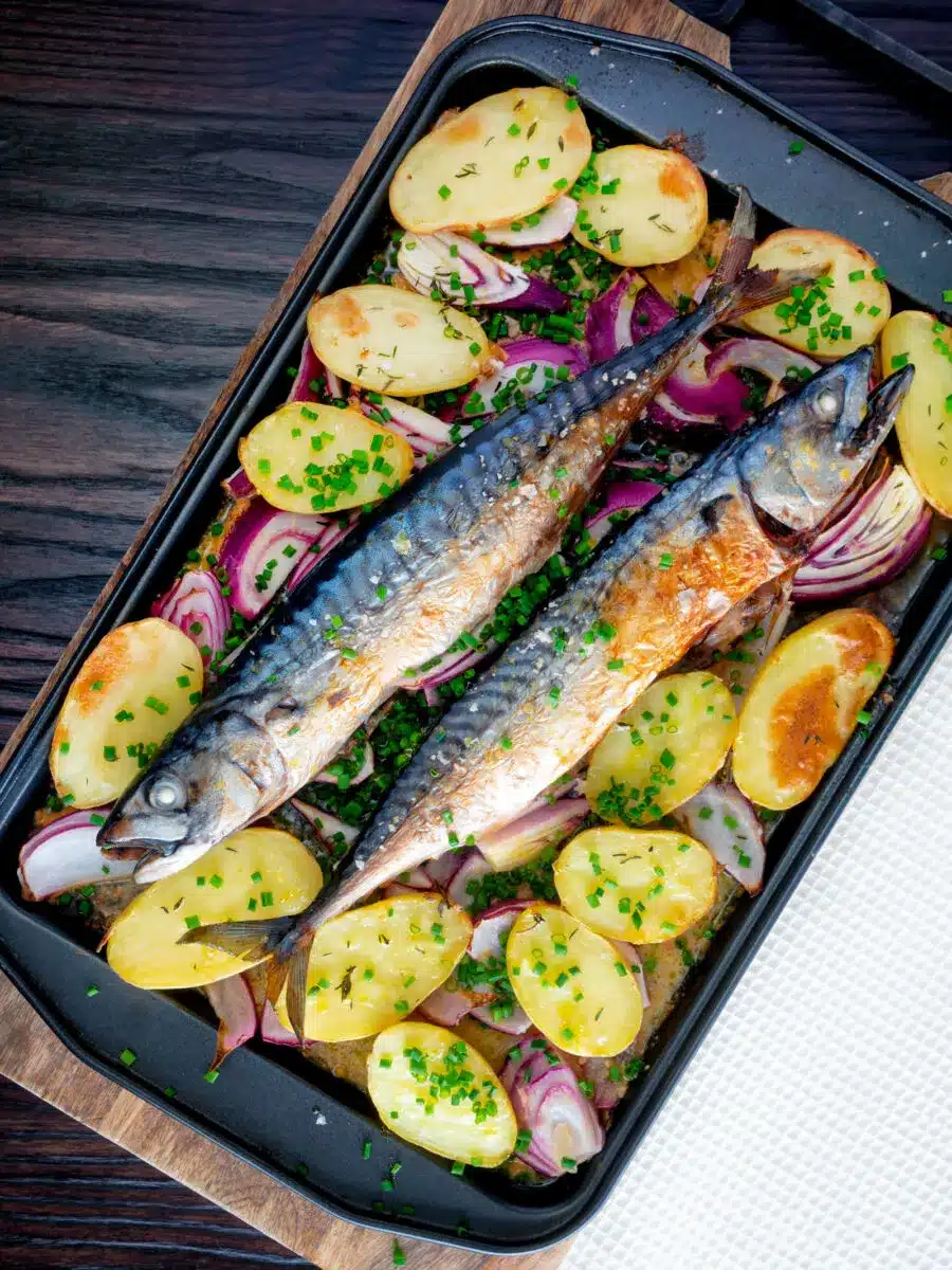 Baked mackerel with potatoes and onions in a black sheet pan.