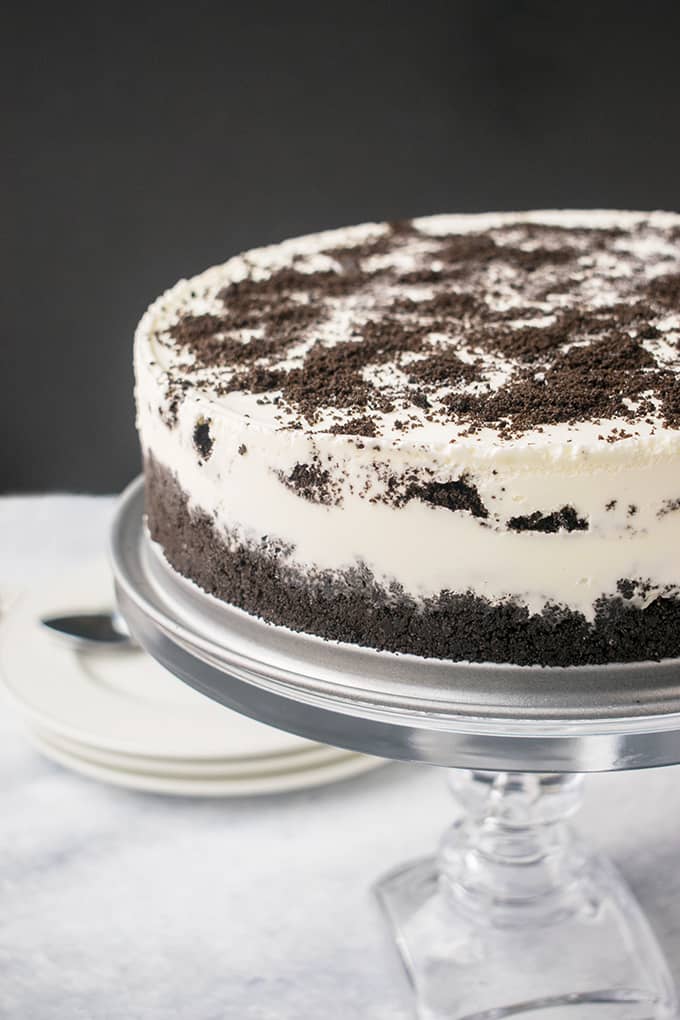 Oreo ice cream cake with caramel on a clear cake stand.