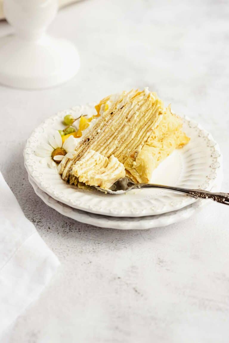 Slice of mango crepe cake on a small plate with a fork.