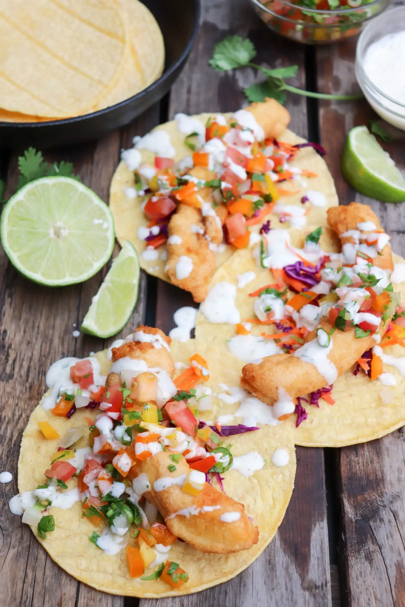 Halibut fish tacos loaded with toppings on a wooden surface.