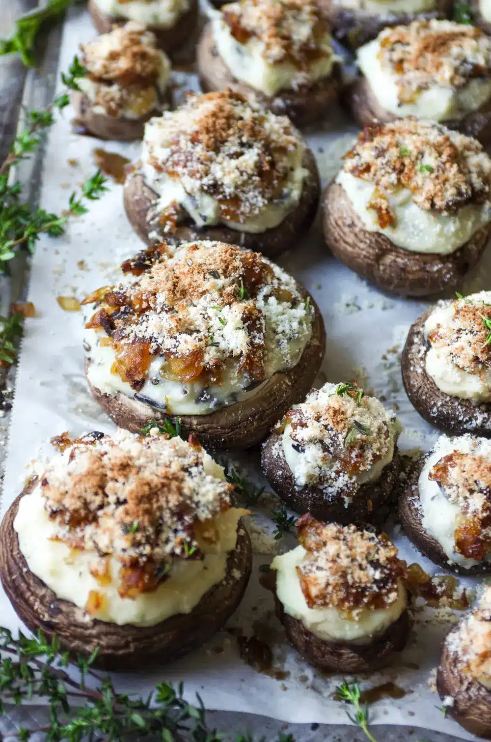 Mashed potato and herb stuffed mushrooms on a parchment paper lined baking sheet.