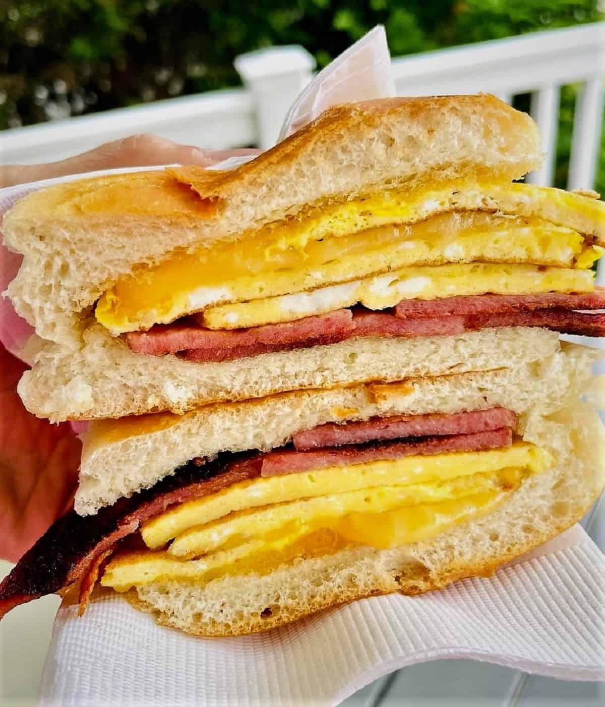 Hand holding pork roll, egg, and cheese breakfast sandwich sliced in half.