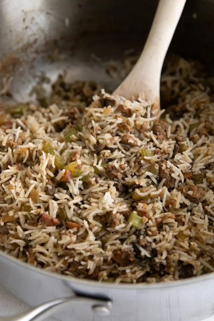 Dirty rice recipe in a skillet with a wooden spoon.