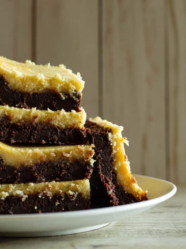 Stack of dark chocolate goat cheese brownies with honey on a white plate.