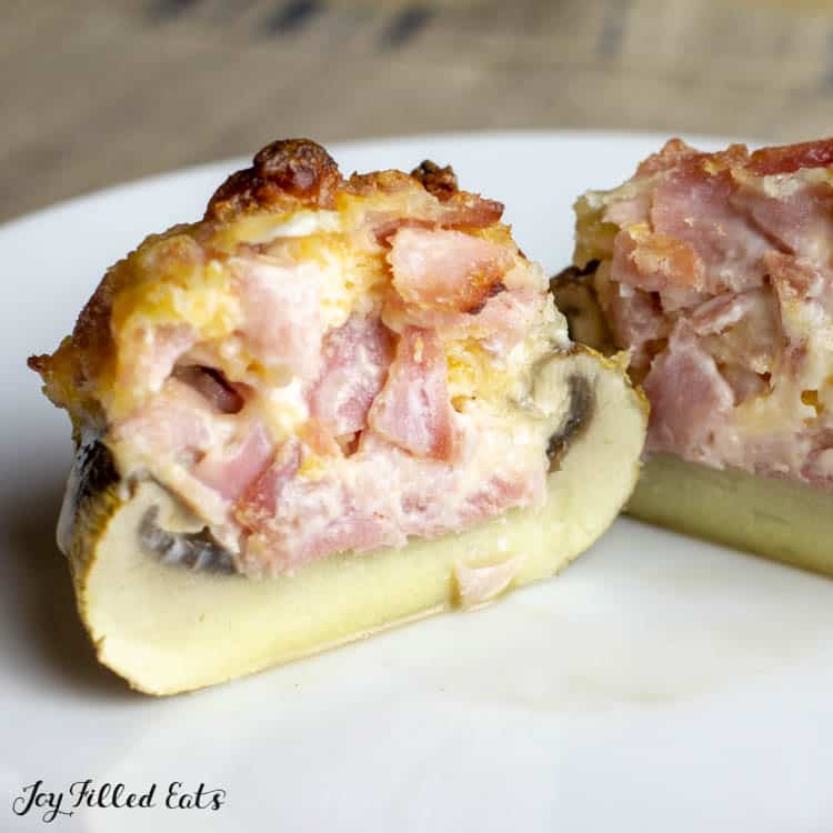 Ham and cheese stuffed mushroom, cut in half on a white plate.