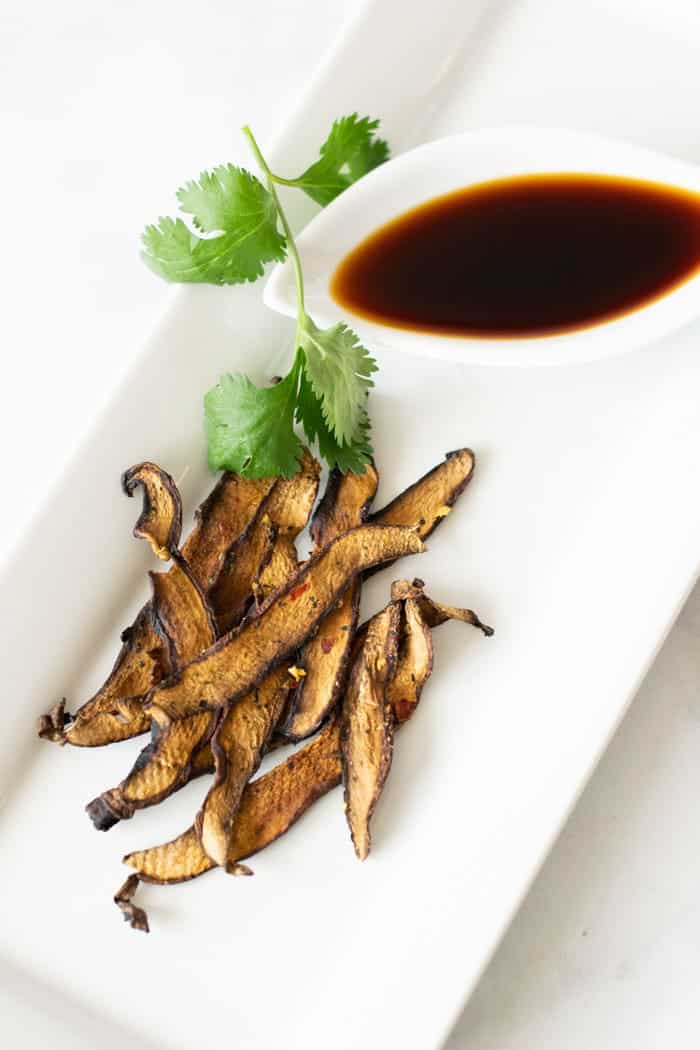 Mushroom jerky with dipping sauce on a white plate.