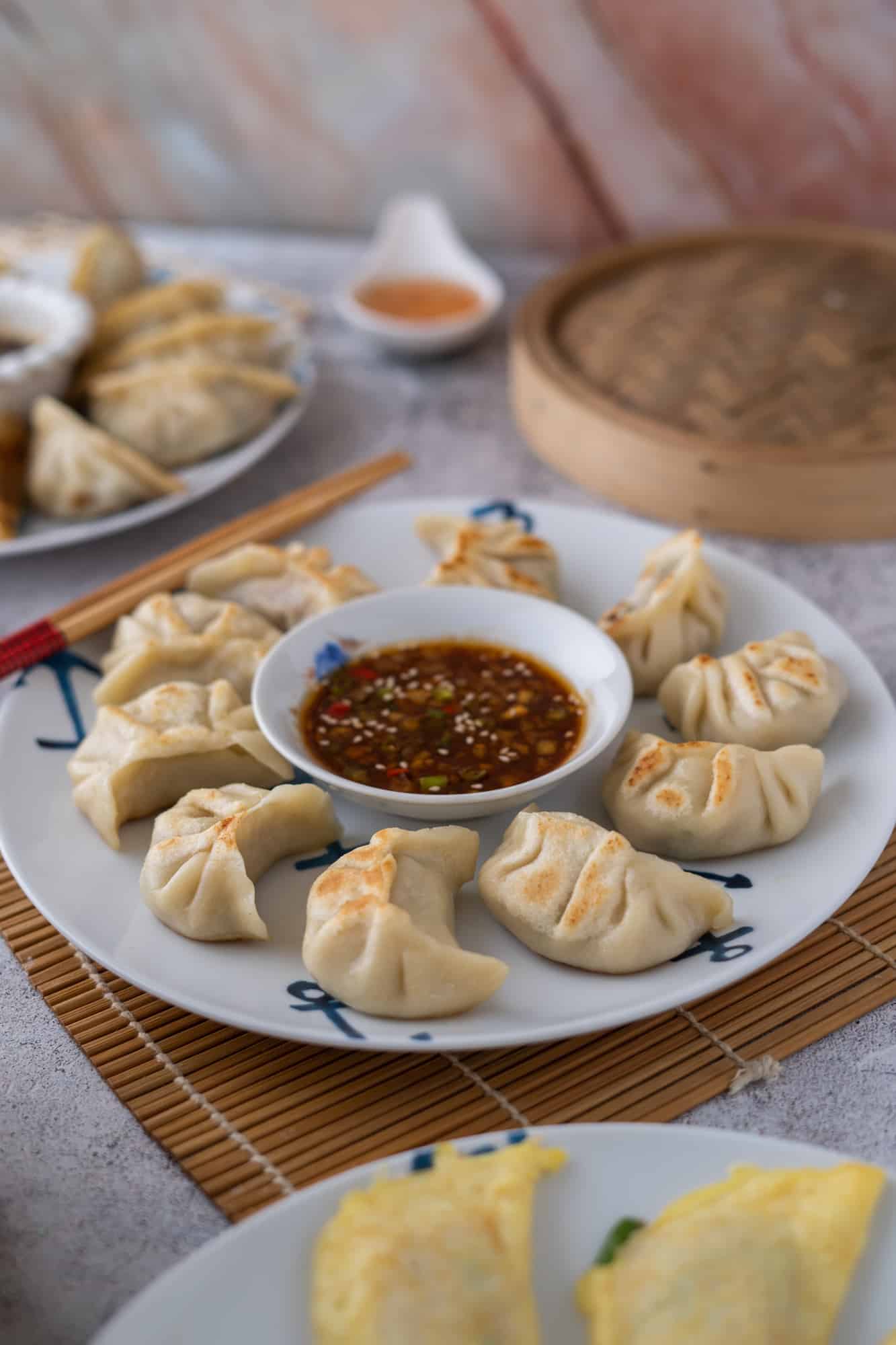 Pork and chive dumplings on a white and blue plate with dipping sauce.