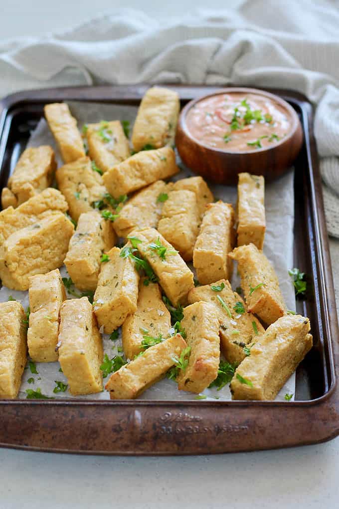 Chickpea fries on a parchment lined baking sheet with dipping sauce.