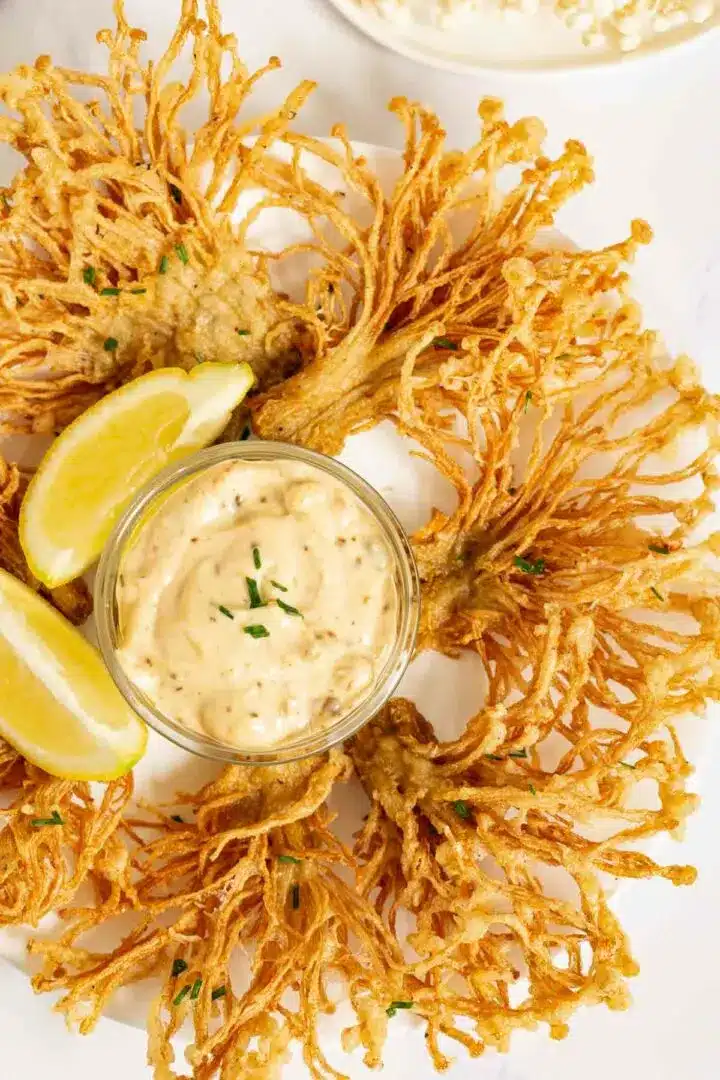 Fried enoki mushrooms with chili aioli on a white plate with lemon wedge.