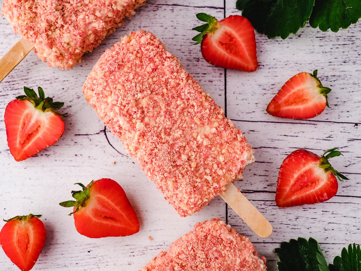 Strawberry shortcake ice cream bars on a white background with sliced strawberries.