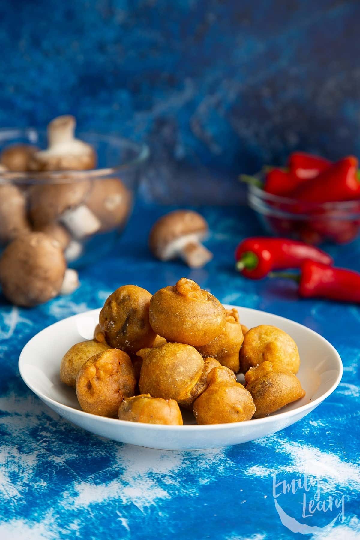 White bowl full of pakora mushrooms with ingredients in the background.