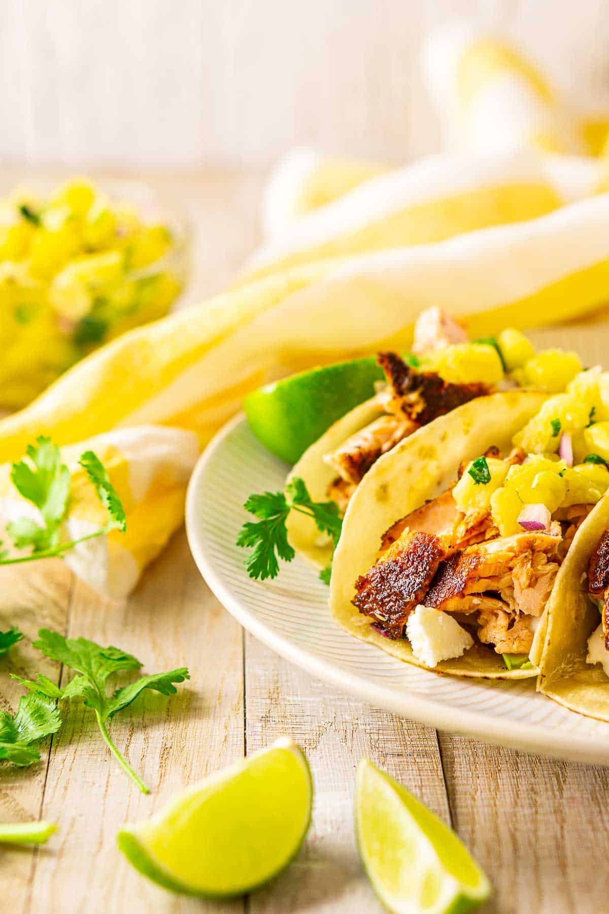 Blackened salmon tacos with pineapple pico de gallo on a white plate with fresh herbs and lime.