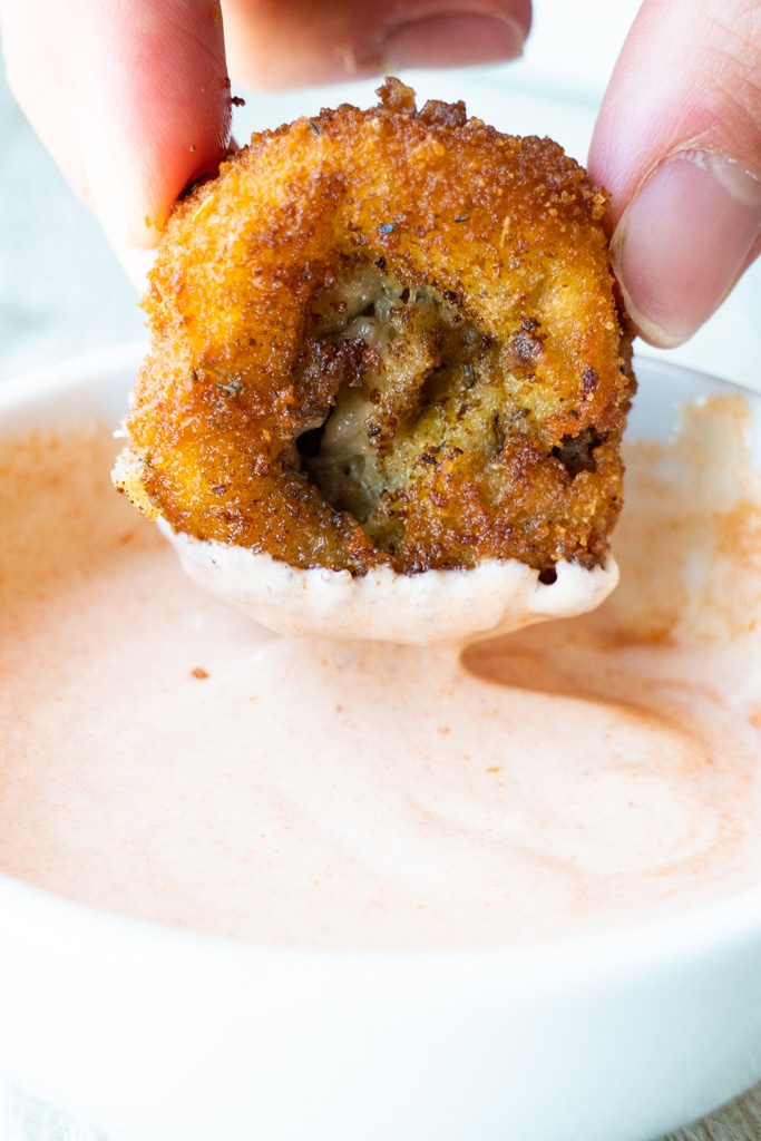 Hand holding breaded mushroom dipping it into sauce.