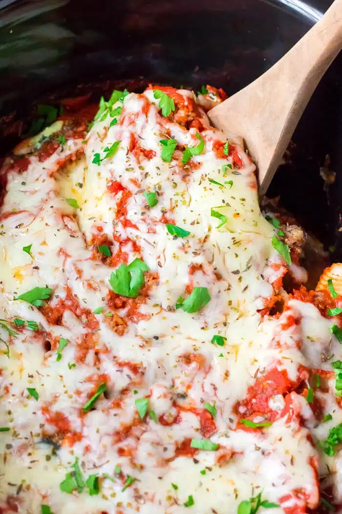 Stuffed shells dish in a crockpot with a wooden serving spoon.