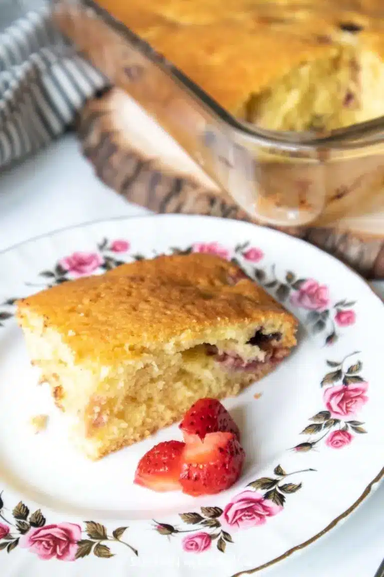 Slice of strawberry sponge cake with chocolate chips on a decorative plate.