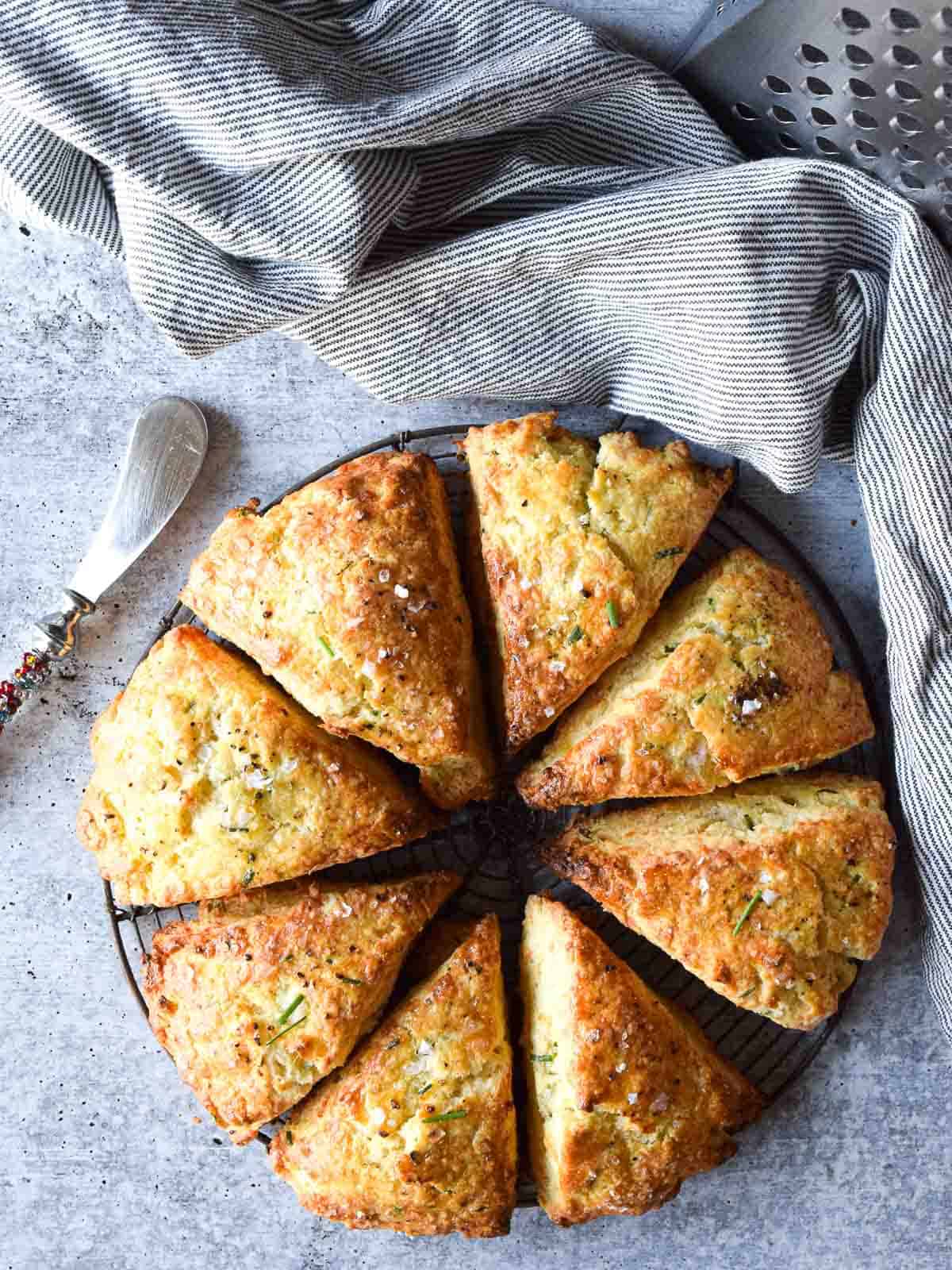 Smoked gouda and chives scones on a cooling rack with butter knife and dish cloth in the background.