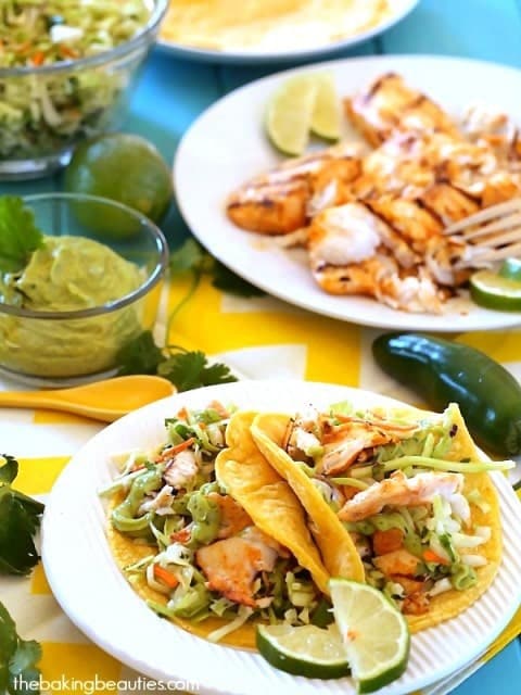 Grilled fish tacos with guacamole, jalapeno, and lime slices on a white.
