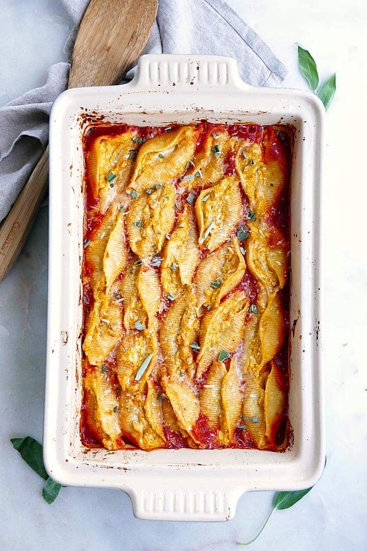 Ricotta pumpkin stuffed shells in a white baking tray with a wooden serving spoon.