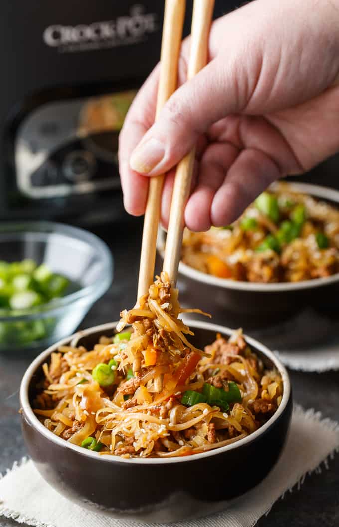 Hand holding chopsticks lifting egg roll in a bowl.
