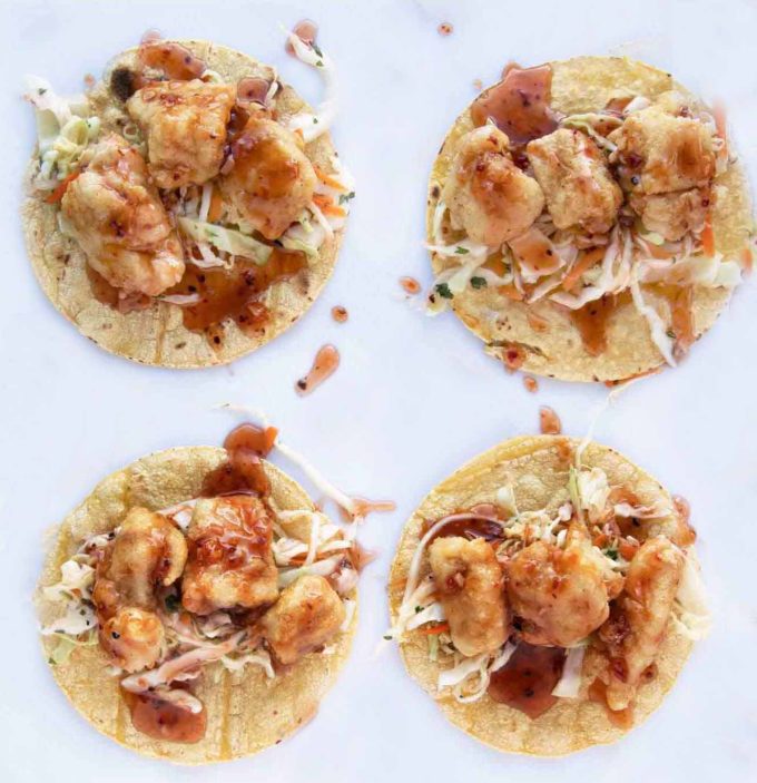 Four Baja-style fish tacos on a white surface.