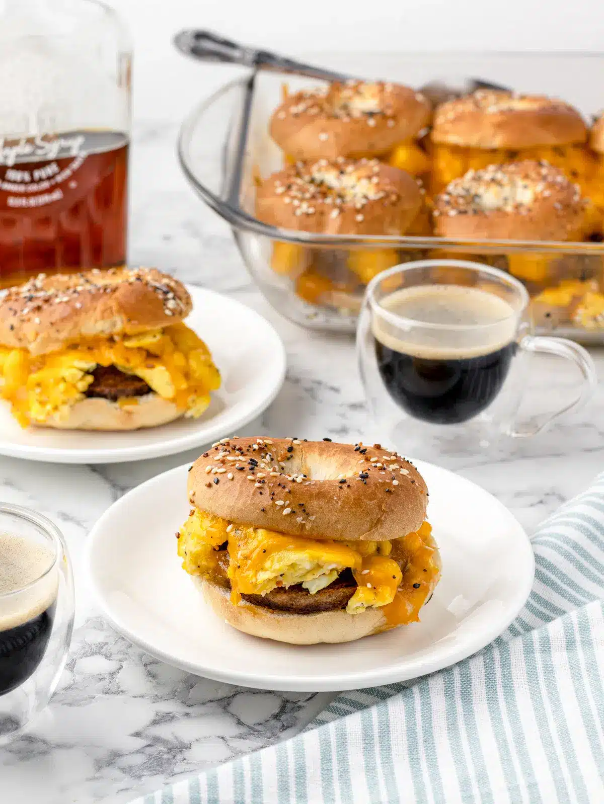 Breakfast bagel sliders in a clear baking dish and one on white plate.