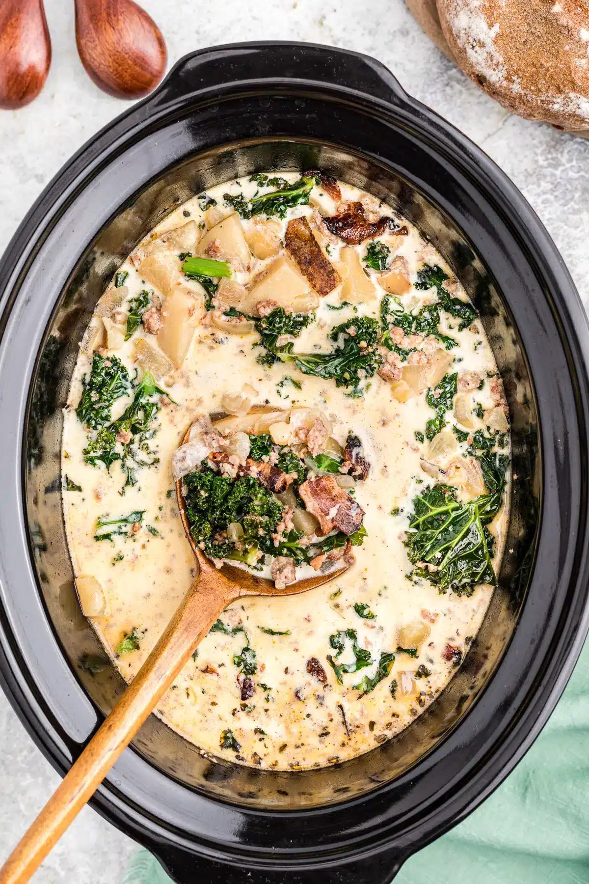 Slow cooker filled with zuppa Toscana soup with spoon inside.