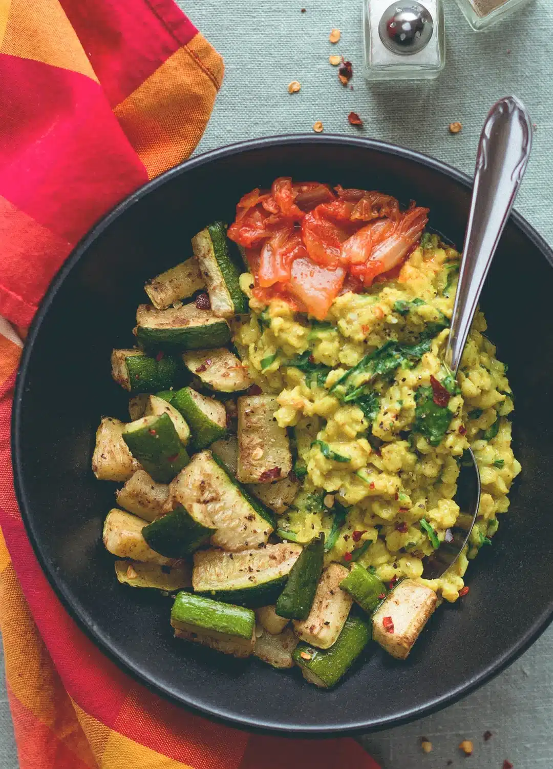 Curry oatmeal with tandoori masala roasted zucchini with kimchi on a black plate.