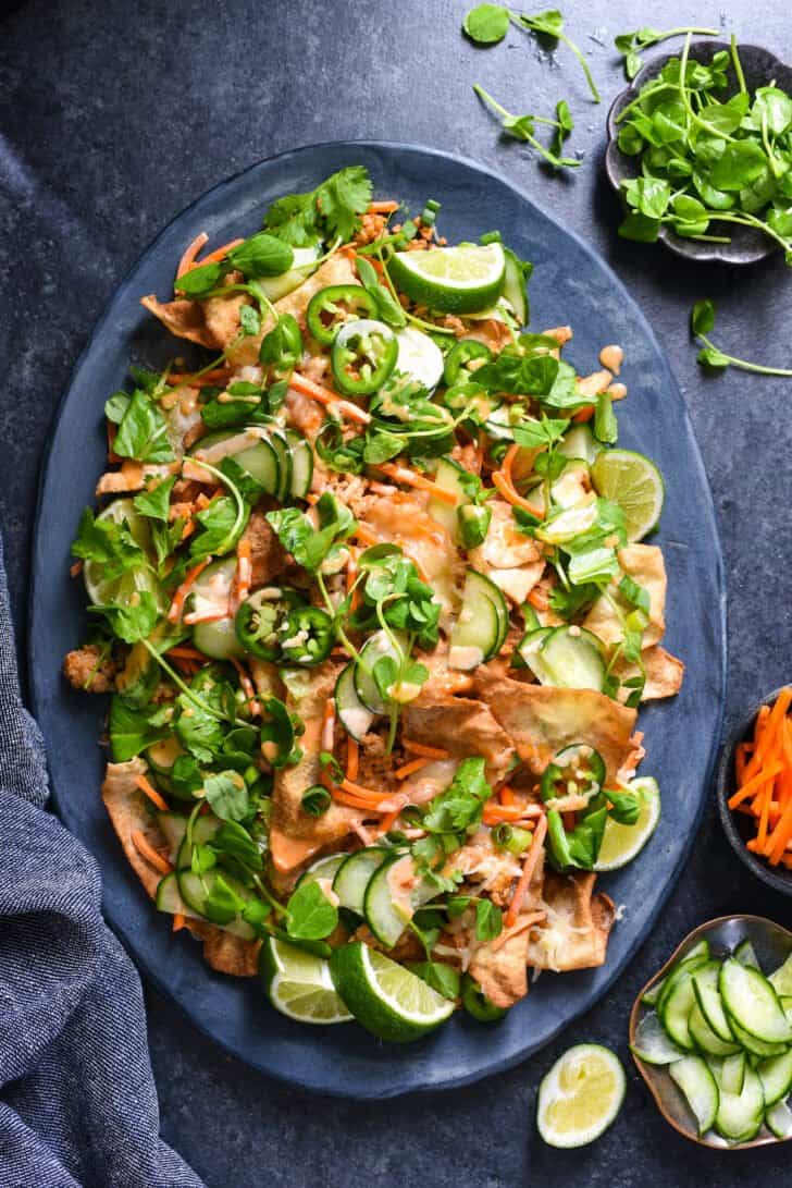 Wonton nachos on a blue serving dish with ingredients surrounding it.