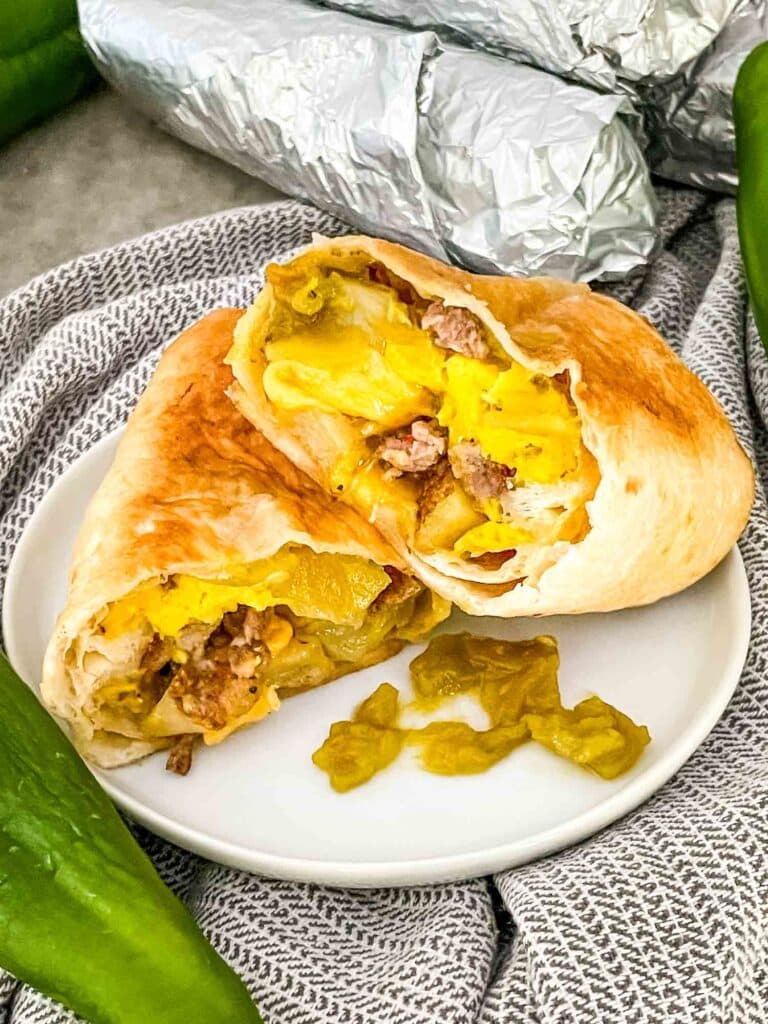 Hatch green chile sausage breakfast burrito cut in half on a white plate.