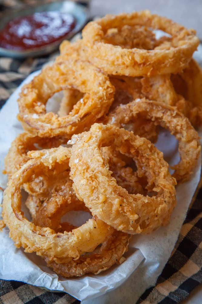 Stack of sourdough onion rings on a white plate with dipping sauce.