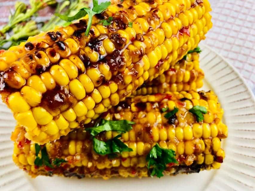 Stack of bang bang grilled corn on the cob on a white plate.