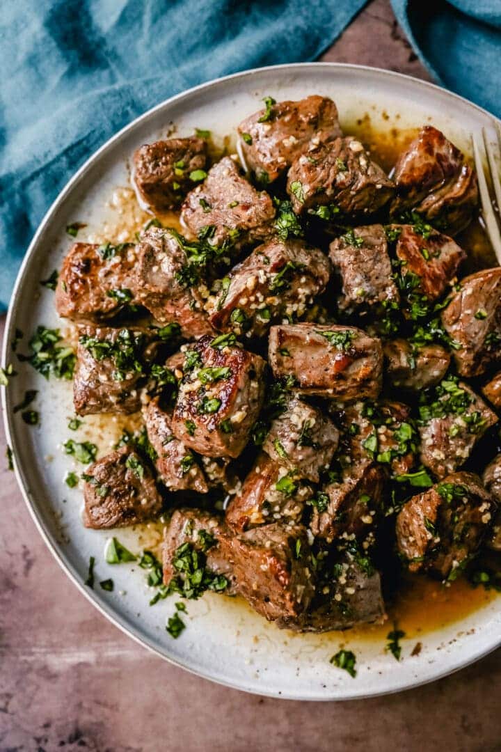 Garlic butter steak bites on a gray plate with blue cloth.