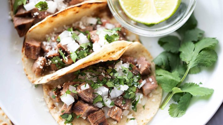 Carne asada street tacos on a white plate.