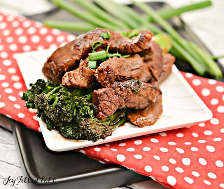 Steak and broccoli stir fry on a square white plate.