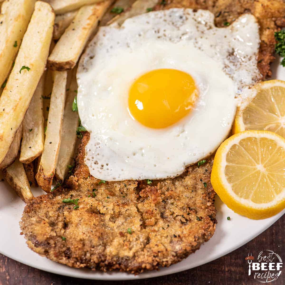 Fried milanesa steak with egg, sliced lemon, and fries.