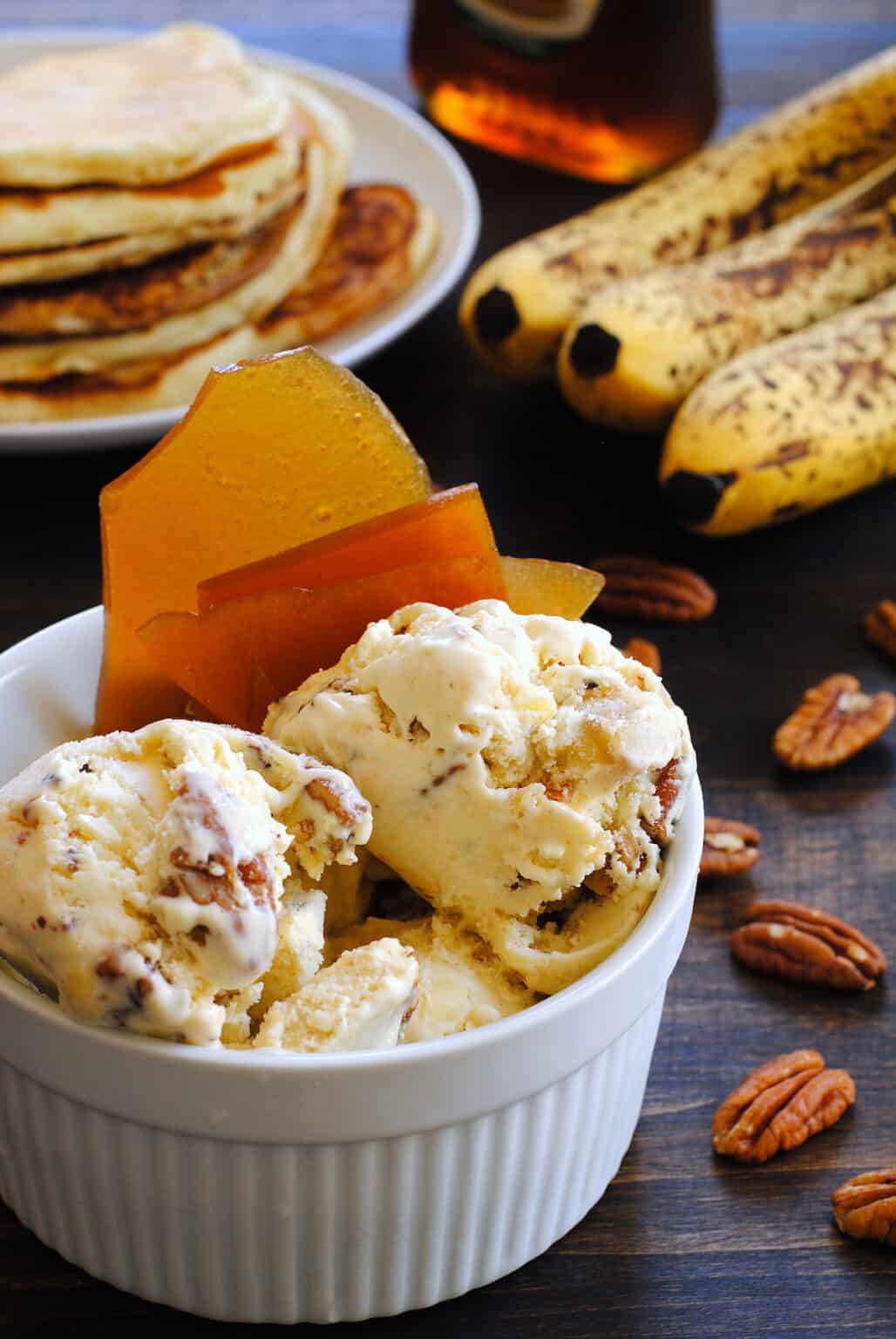 Banana pancake ice cream with maple brittle and bananas, pecans, and pancakes in the background.