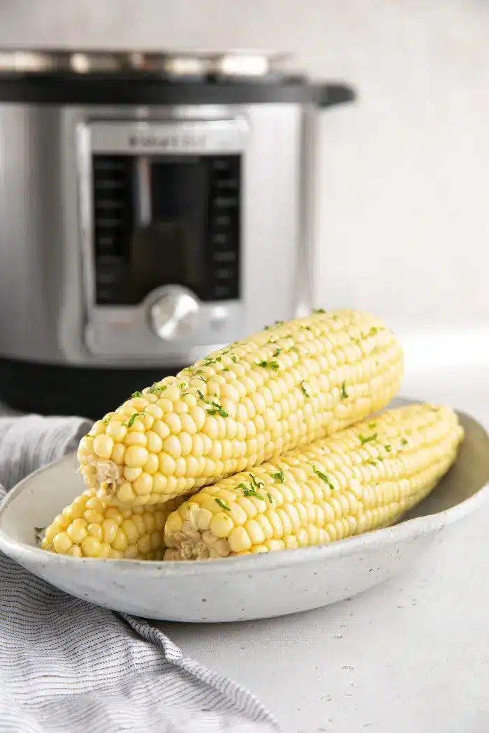 Corn on the cob in a bowl with Instant Pot in the background.