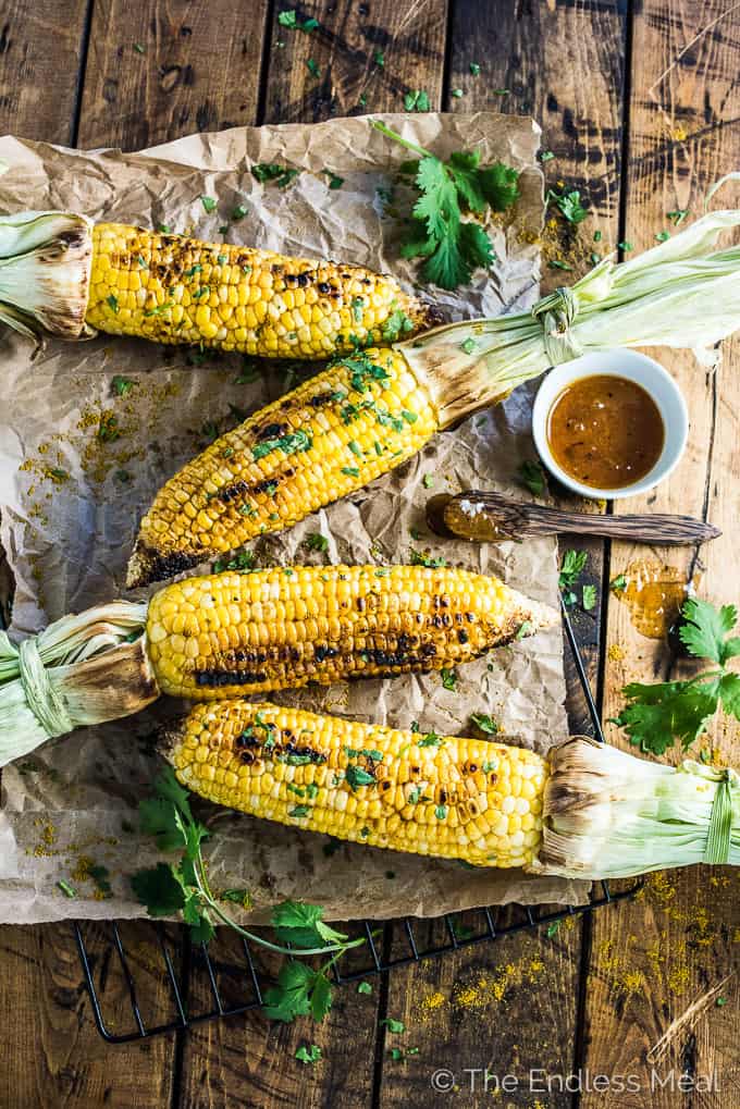 Roasted corn on the cob on parchment paper with a small bowl of mango chutney butter.
