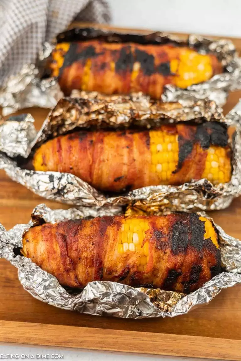 Bacon wrapped corn on the cob in aluminum foil.